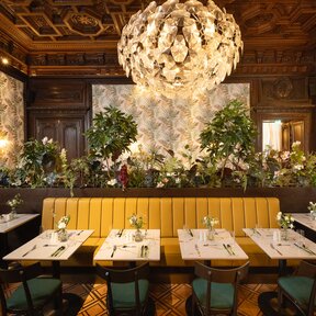 Bel étage with set tables, lush greenery and chandeliers