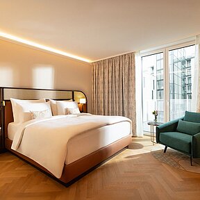 Hotel room with king-size bed, green chair, and view of the Inner Courtyard