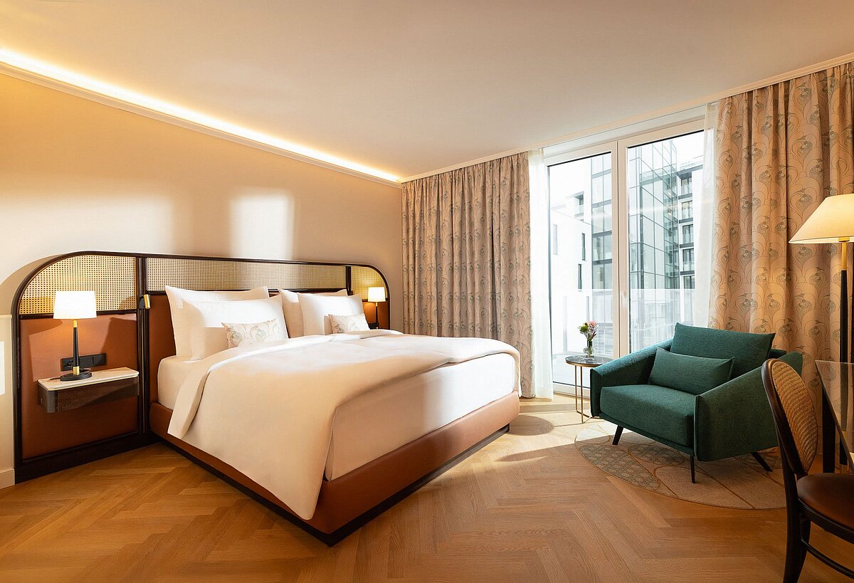Hotel room with king-size bed, green chair, and view of the Inner Courtyard