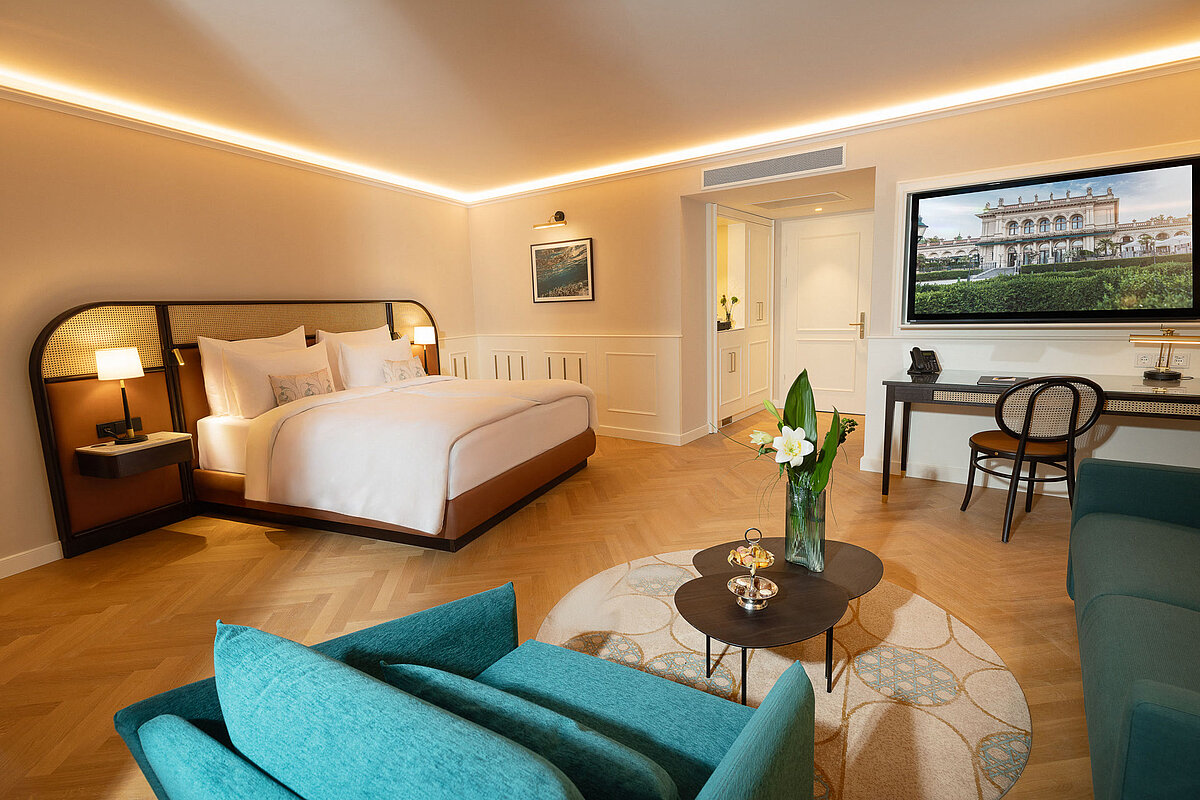 Spacious hotel room featuring a sofa, chair, working desk, and smart TV
